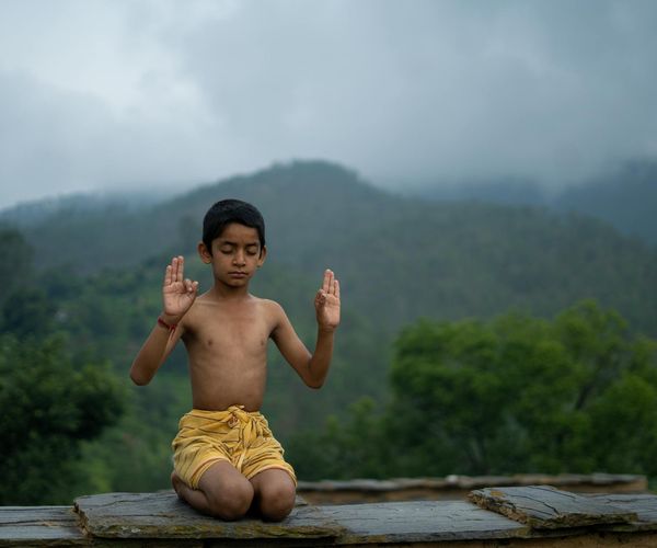 Persona realizando una postura de equilibrio de yoga con un paisaje sereno de fondo.